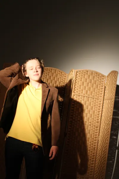 J.J. Barton with a brown jacket slung over one shoulder and his eyes closed, smiling, in a yellow polo shirt.