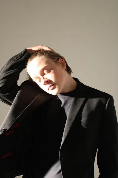 J.J. Barton running a hand through his hair, head tipped back with eyes closed, in a dark jacket.