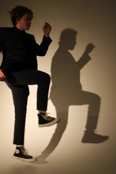 J.J. Barton with one knee raised and a fist up, his silhouette thrown large on the wall behind him.