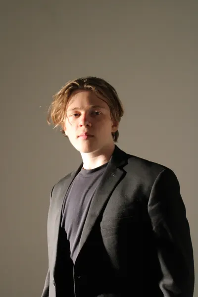 J.J. Barton standing and facing the camera in a dark blazer over a grey tee shirt.