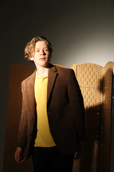 J.J. Barton standing facing the camera in a brown jacket and yellow polo, woven screens behind him.