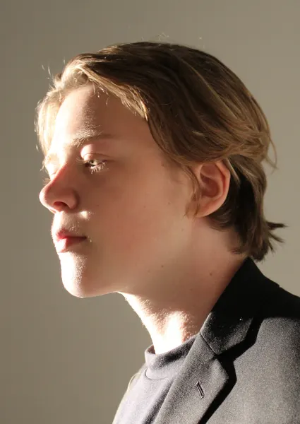 Close profile portrait of J.J. Barton in sunlight, looking off to his right, wearing a grey jacket.